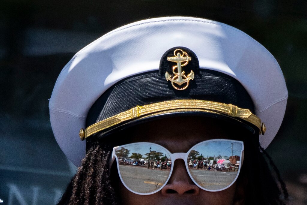 The Blue Angels complete their annual fly over Annapolis during the Naval Academy's commencement week on May 22, 2024. A Naval Academy member watches the protest against climate change from across the street.