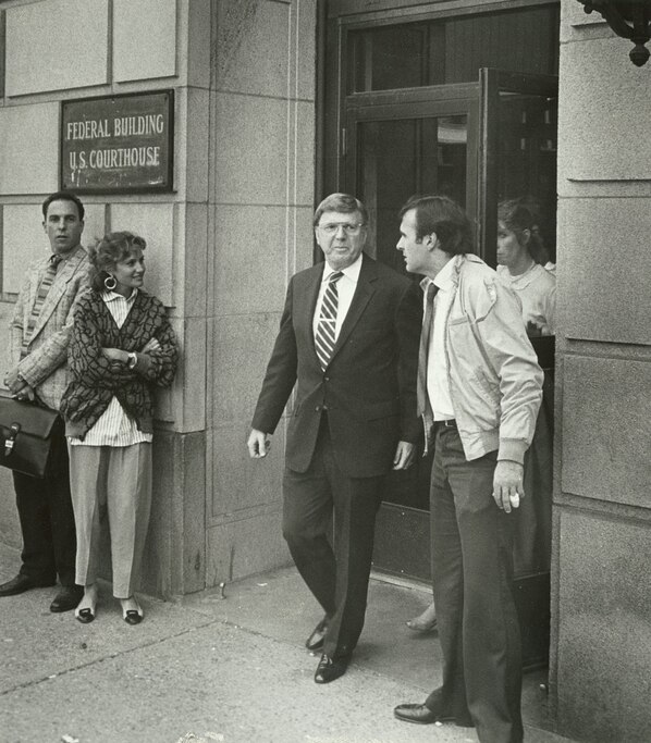 Black and white photograph of Carl Stevens exiting door of a federal courthouse, flanked by various people on left and right of the doors.
