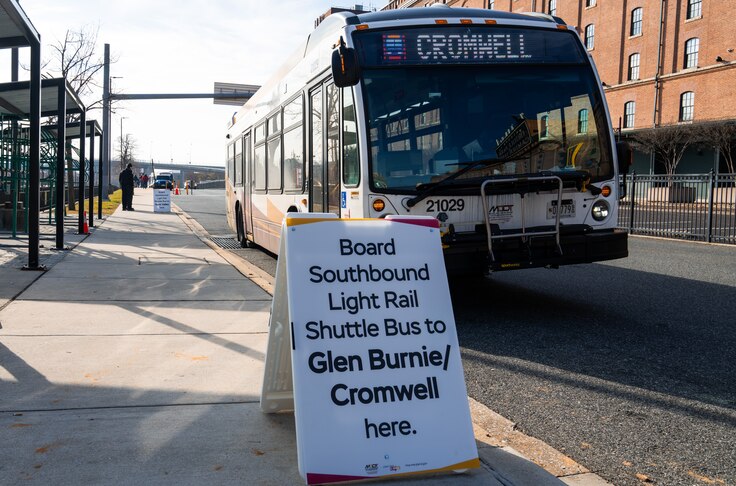 A southbound shuttle bus pulls up in front of a sign reading "Board Southbound Light Rail Shuttle Bus to Glen Burnie/Cromwell here."