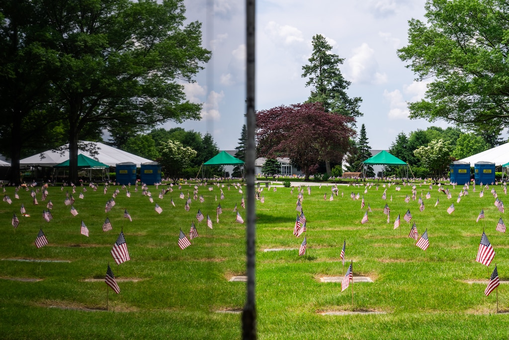Flags placed by members of the Young Marines and Girl Scouts marking the gravesites of veterans are reflected in a statue at Dulaney Valley Memorial Gardens in Timonium on May 25, 2024.