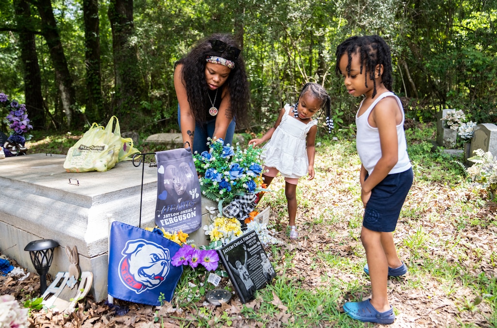 Doni Smith tidies up around the grave of her fiancé, Jaylon Ferguson, with their children Jrea and Jyce Ferguson at St. Paul No. 1 Cemetery in St. Francisville, Louisiana, on June 21, 2023.