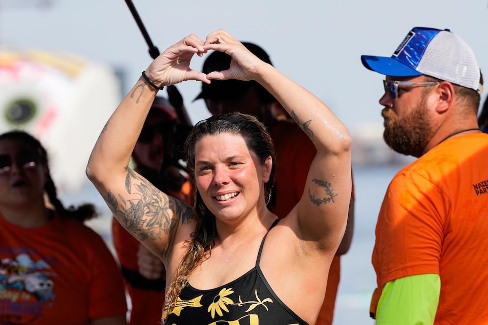 Katie Humphrey holds up a hand heart to her supporters after completing her 24-mile swim at the Inner Harbor.
