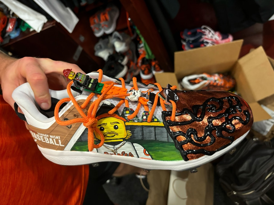 Gunnar Henderson holds his custom cleats by Soles By Sir, featuring Lego characters and Henderson's face.