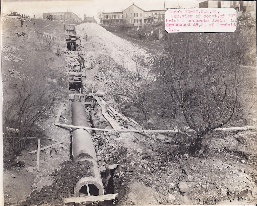 An archived black and white photograph of an underground pipe being constructed and buried.