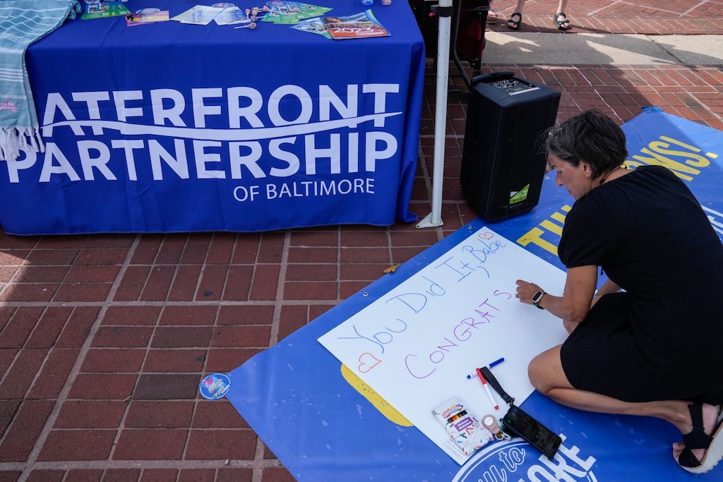 Cindy Freeman, a friend of Katie’s and fellow swimmer, makes a sign to show her support at Waterfront Partnership’s table at the Inner Harbor amphitheater.
